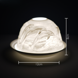 Cello porcelain tealight holder dome featuring a dolphin design with dolphins leaping out of the ocean. Dimensions: 8cm height, 12cm width, displayed against a dark background.