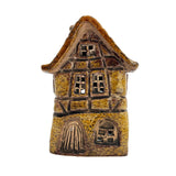 Front view of the Briarwood Hollow yellow pottery house tealight holder with glowing windows and storybook-style cottage design.