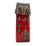 Front view of the Scribe’s Retreat village pottery house with softly glowing LED light shining through arched windows and rustic red brickwork.