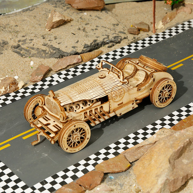 Wooden ROBOTIME ROKR Models Grand Prix Car on a checked racing track with natural landscape in the background