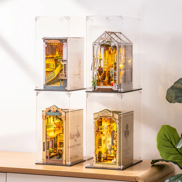 Four illuminated model book nooks in ROBOTIME Rolife Book Nook Dust Cover WD1001 on a wooden surface.