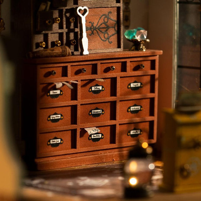 ROBOTIME Rolife Kits Kiki's Magic Emporium DIY Miniature House Kit - DG155 lifestyle - Wooden apothecary cabinet with various items on top in a softly blurred background