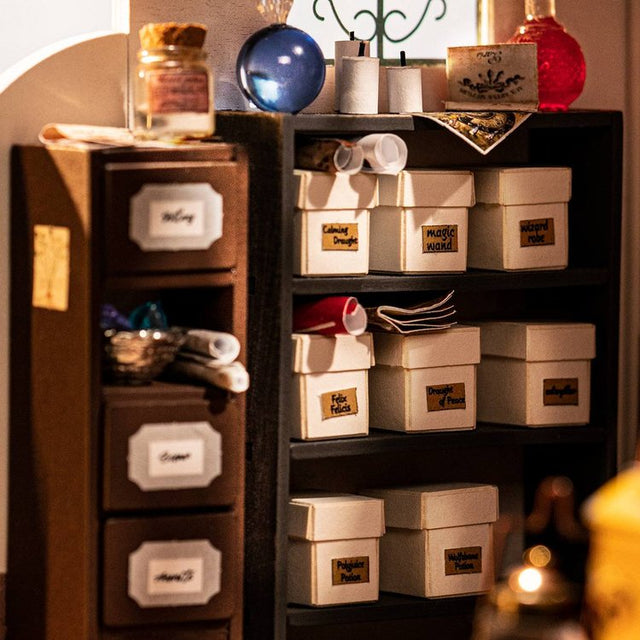 ROBOTIME Rolife Kits Kiki's Magic Emporium DIY Miniature House Kit - DG155 detail: Shelf with labeled boxes and decorative items in a warm, indoor setting