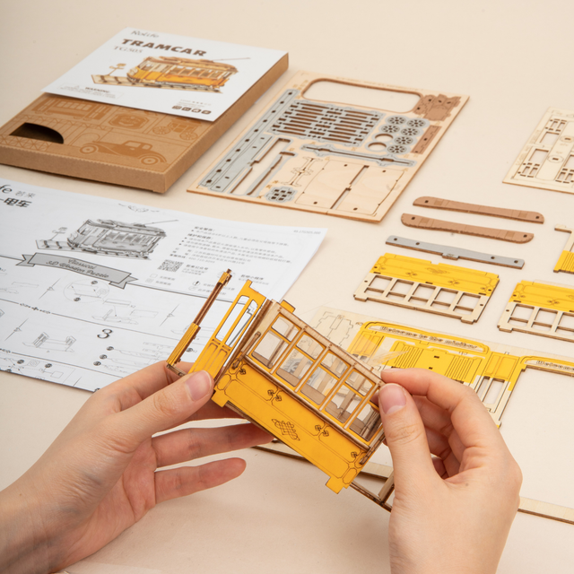 Wooden ROBOTIME Rolife kits Tramcar with assembly pieces and instructions on a table.