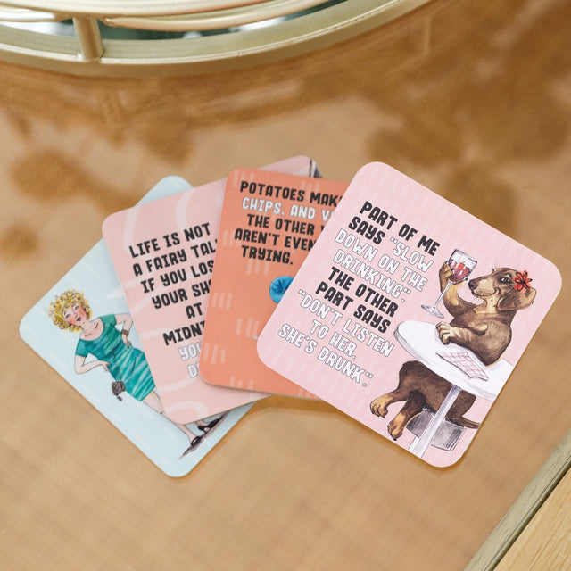 Set of four drinks coasters with humorous illustrations and text on a wooden surface.