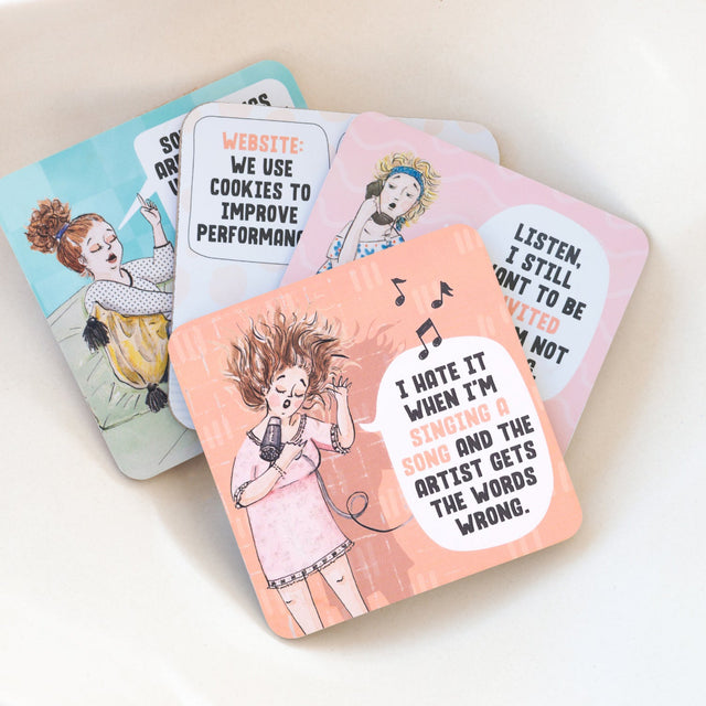 Set of four drinks coasters with illustrated characters and humorous text on a light background