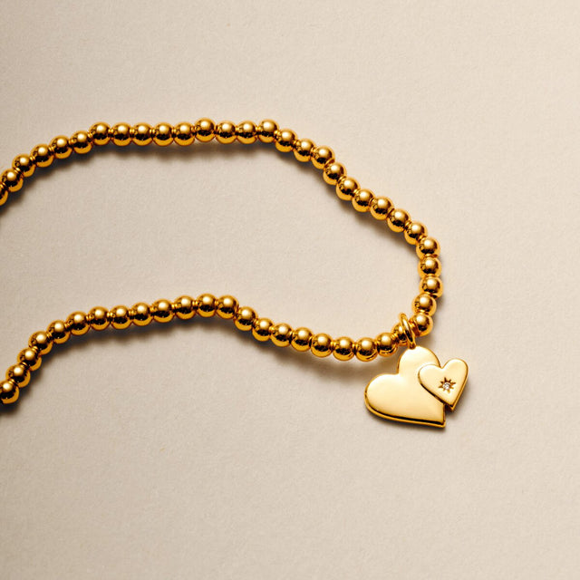 Gold plated beaded bracelet with two linked heart charms