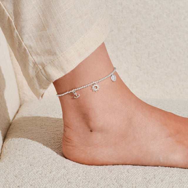 Silver charm anklet worn on ankle with delicate beaded stretch design