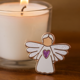 Angel of Prayer guardian angel pin displayed beside a lit candle, symbolising peace, reflection, and faith.