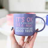 Person holding Splosh Cheeky Mug Good Taste, purple mug with humorous quote, perfect witty gift for friends or coworkers.